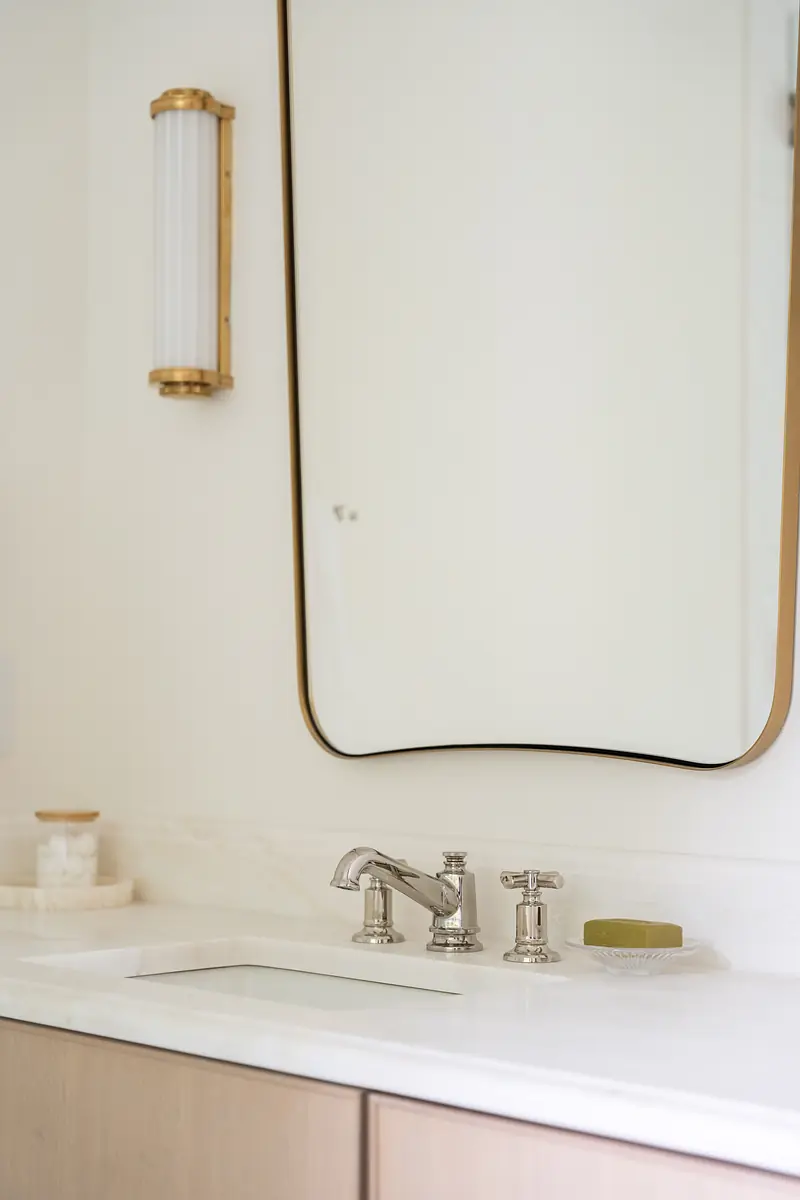 Bathroom with white countertop, chrome faucet, large gold-framed mirror, and light wood cabinetry.