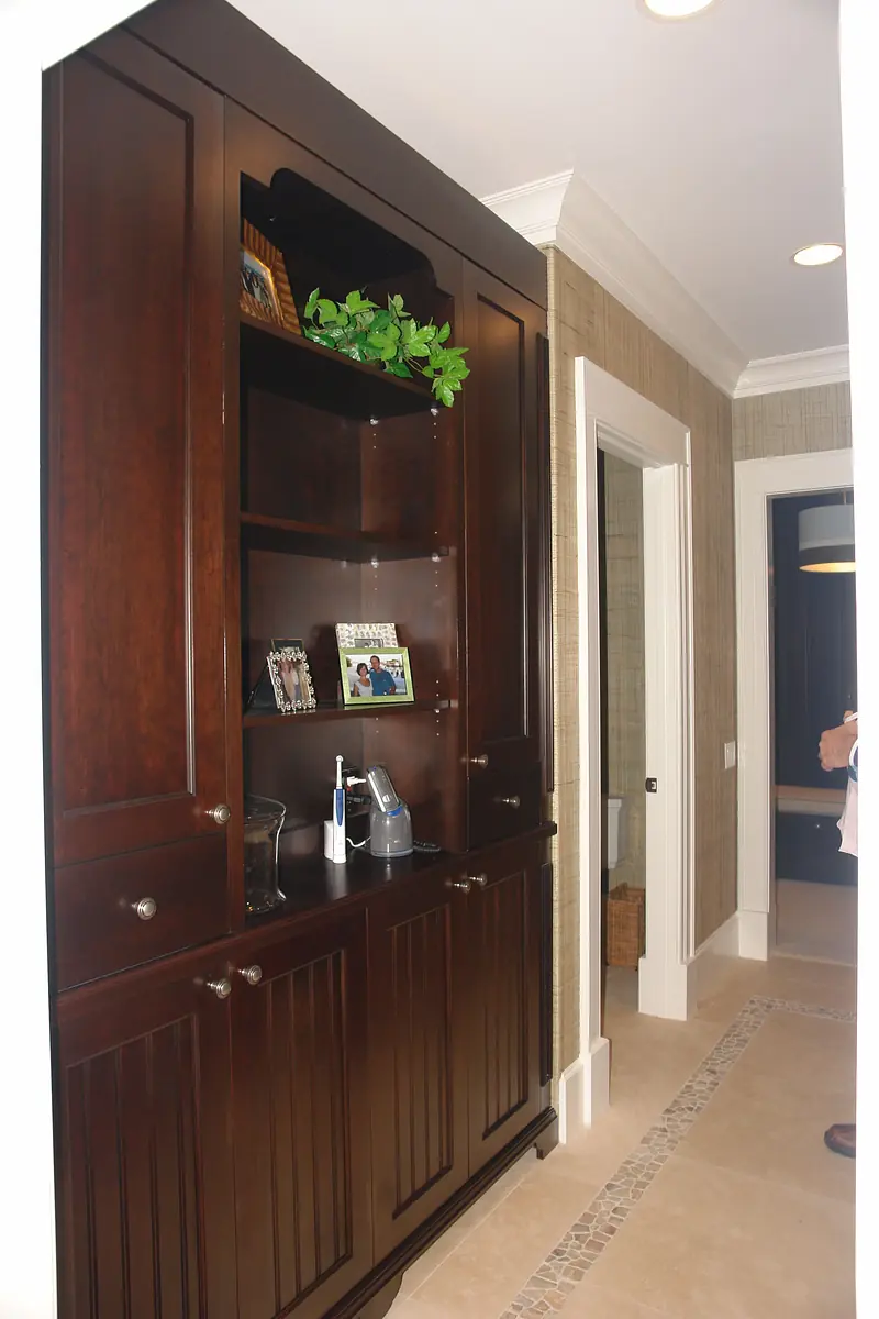 Hallway with dark wooden cabinet, photographs, decorative plant, and textured wallpaper.