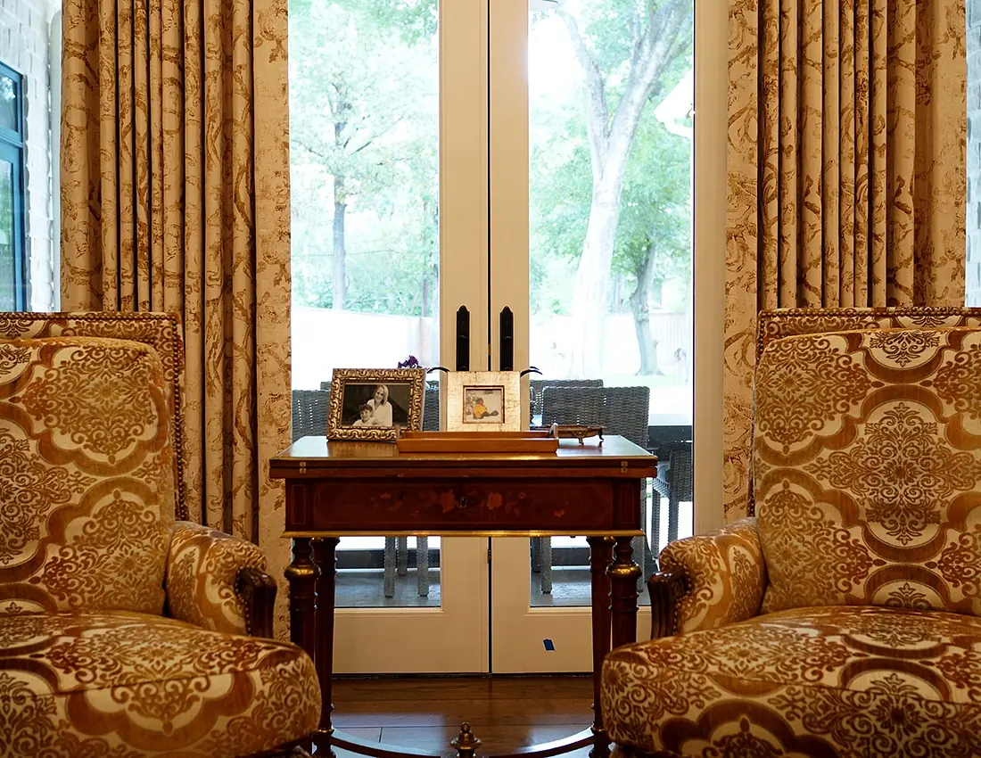 Living room with upholstered chairs, wooden table, framed photographs, and glass doors to outdoor area