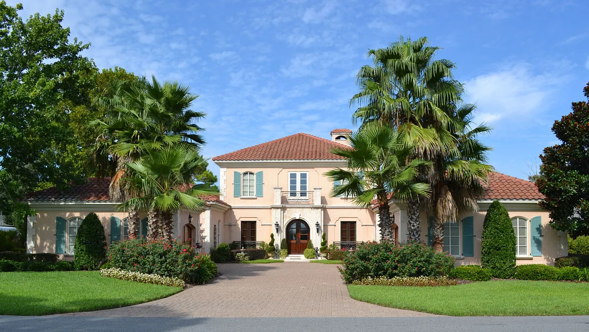 Front exterior of a house with stucco facade, red-tiled roof, palm trees, and paved driveway.