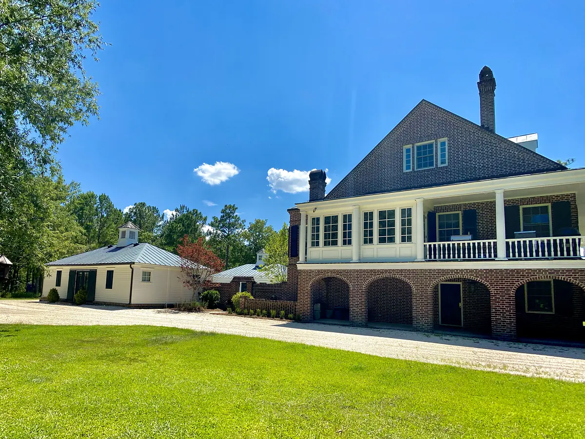 Exterior view of a two-story house with balconies, brick, siding, lawn, and gravel driveway.