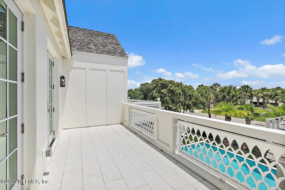 Outdoor deck with white tiles, decorative railing, and views of greenery and water.