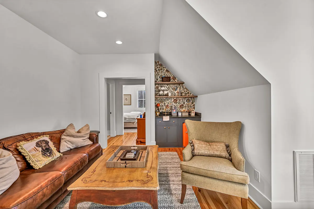 Living room with brown leather sofa, beige armchair, wooden coffee table, and patterned wall shelf.