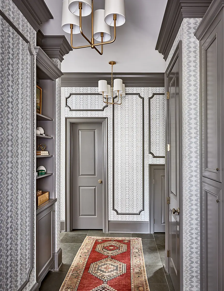 Hallway with patterned wallpaper, runner rug, built-in cabinetry, and molding details.