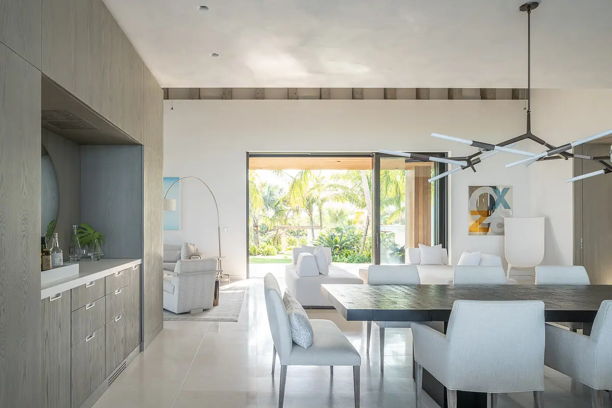 Dining room with rectangular table, white chairs, sideboard, and sliding glass doors to garden view