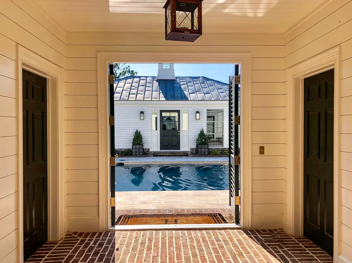 Foyer with brick flooring, green doors, shiplap walls, and a lantern, leading to an outdoor pool area.
