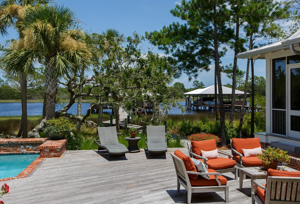 Outdoor deck with orange chairs, wooden table, spa, and views of water and palm trees.