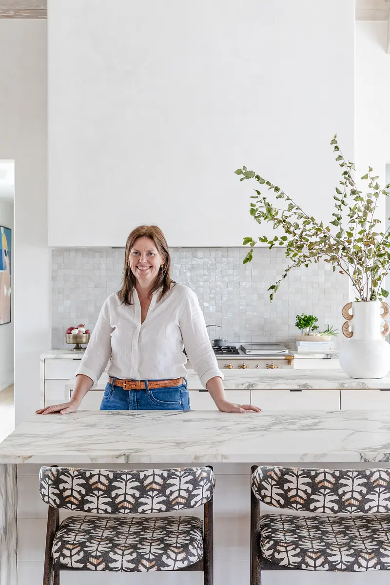 Kitchen with marble island, patterned bar stools, white tile backsplash, and a vase with greenery