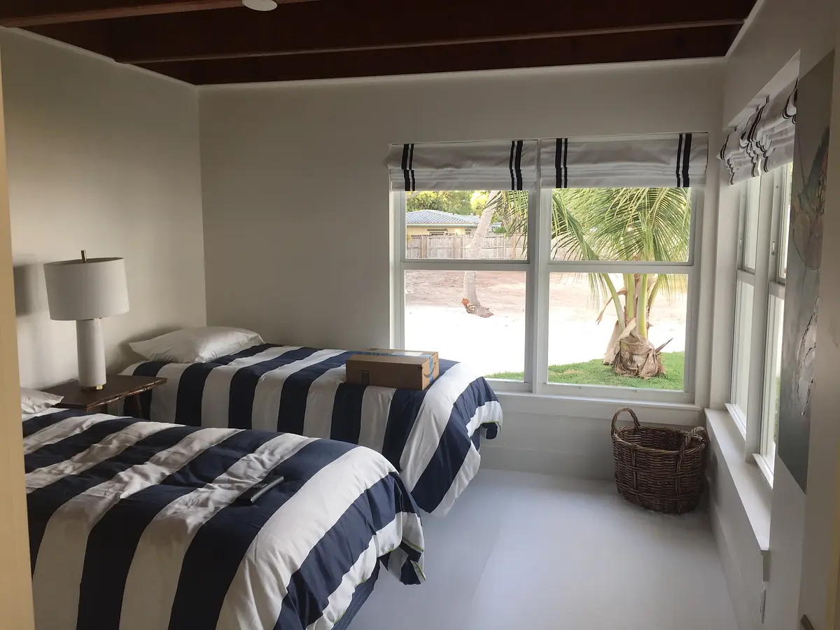 Bedroom with twin beds, navy and white striped bedding, bedside lamp, and large window with greenery outside.