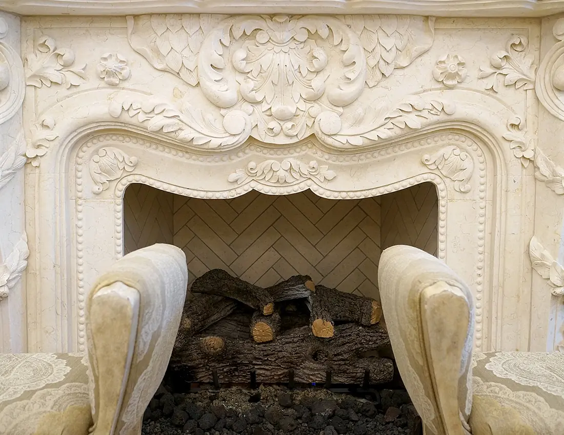 Living room with ornate stone fireplace and two upholstered chairs in front.