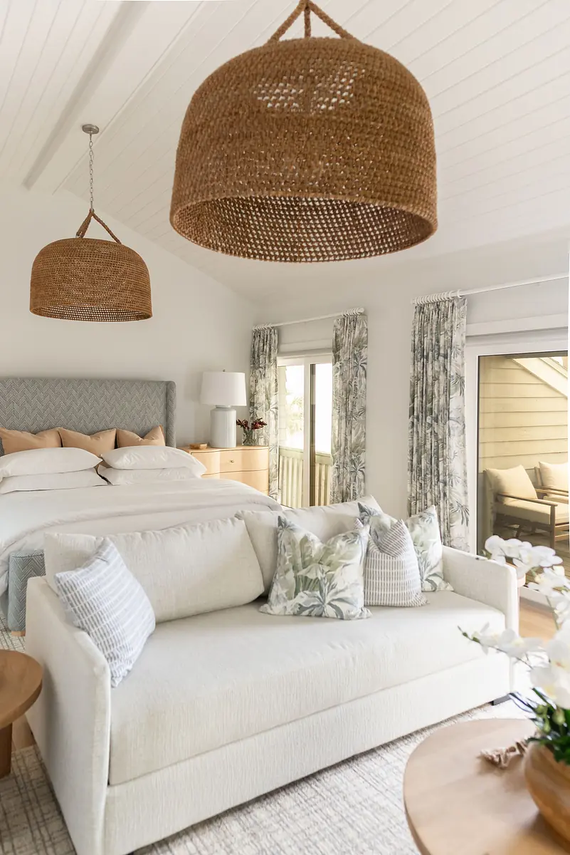 Bedroom with large bed, white sofa, floral pillows, woven pendant lights, and sliding door to the patio