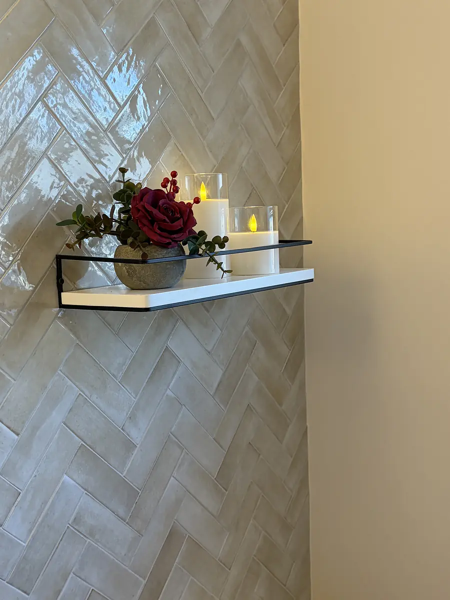 Wall-mounted shelf with candles and flower arrangement on herringbone tile wall