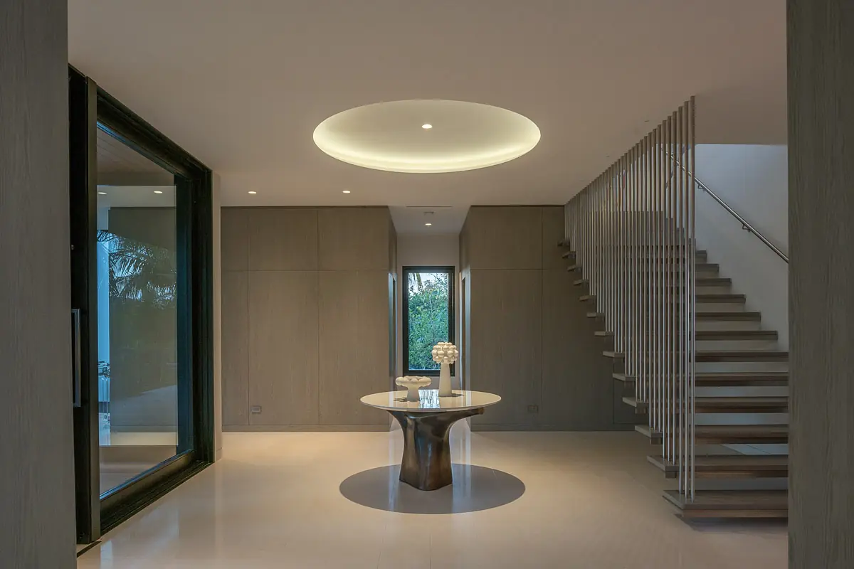 Foyer featuring a round table, decorative object, large windows, wooden staircase, and circular ceiling light.