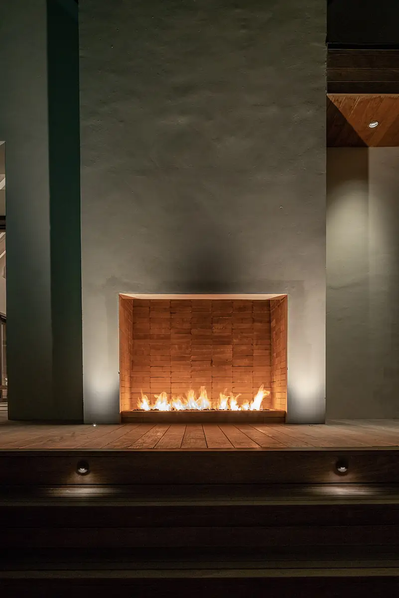Exterior space with recessed wood fireplace and wooden deck, featuring subtle lighting along walls and deck