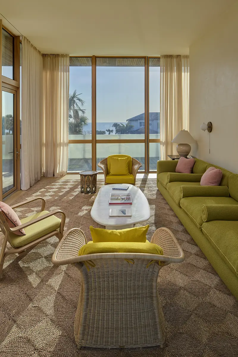 Living room with light green sofa, armchairs, white coffee table, and large windows with sheer curtains.