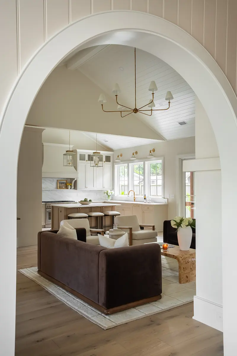 Living room with brown sofa, area rug, round table, dining area, large windows, and white beamed ceiling