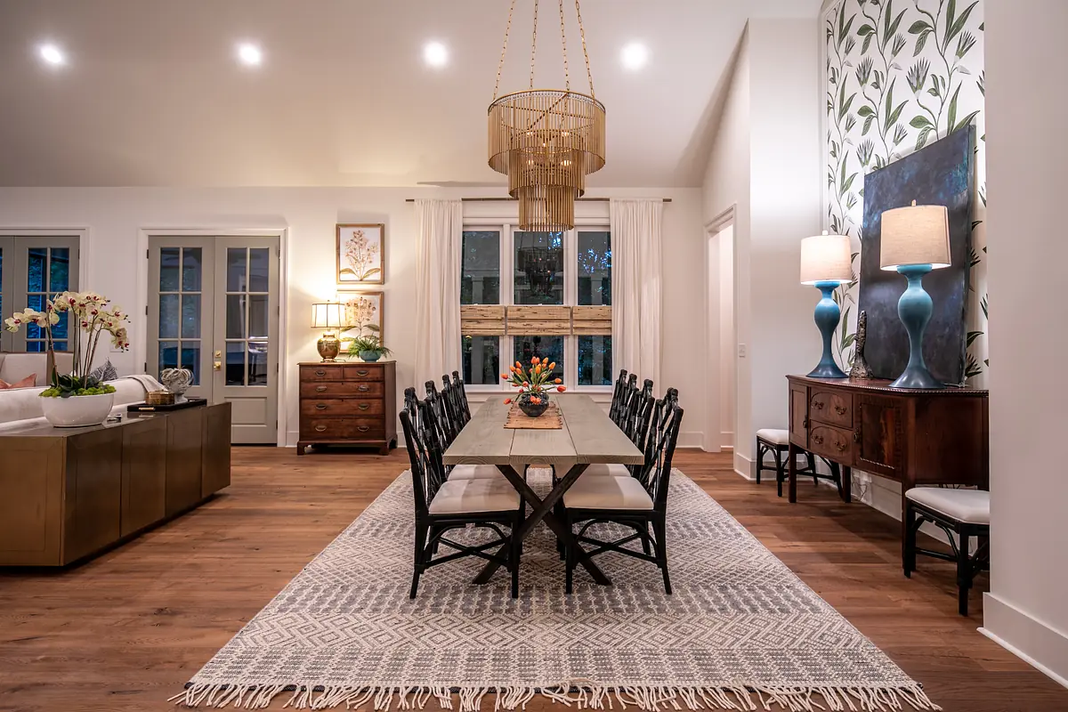 Dining room with rectangular table, black chairs, patterned rug, decorative lamps, and sideboard with natural light.