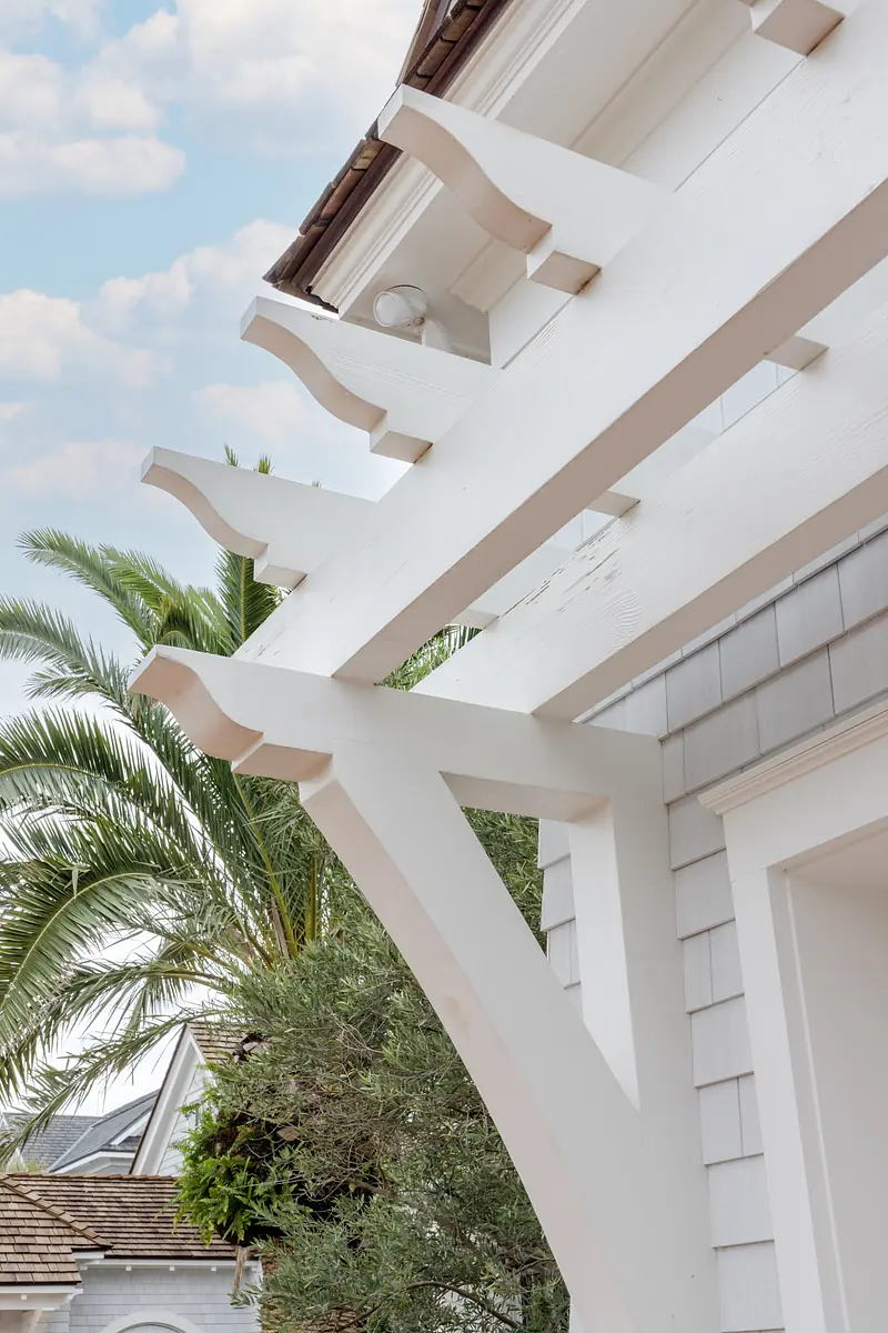 Exterior front view with gabled roof, light gray shingles, decorative pergola, and palm trees