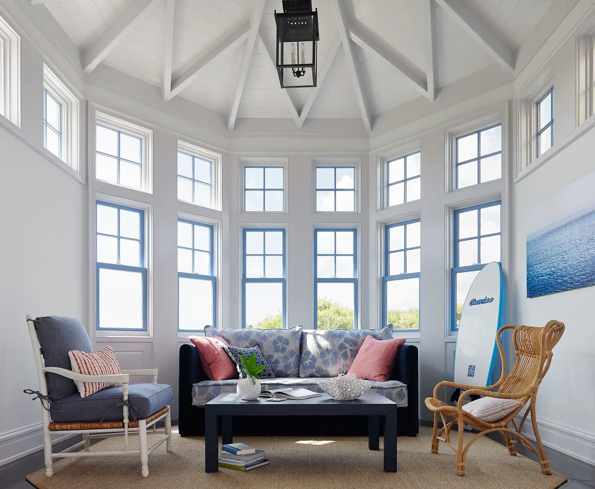 Living room with black sofa, floral cushions, grey armchair, rattan chair, coffee table, and multiple windows.