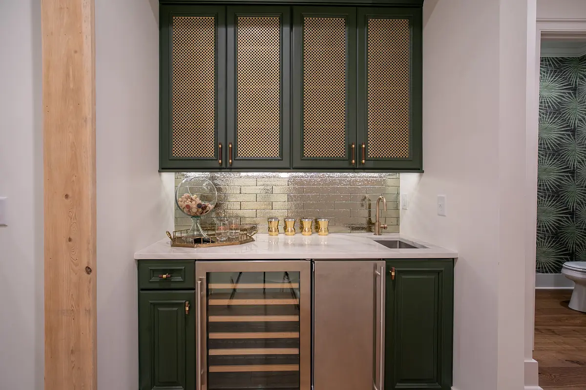 Butler's pantry with dark green cabinets, marble countertop, stainless steel sink, wine cooler, and silver brick backsplash.