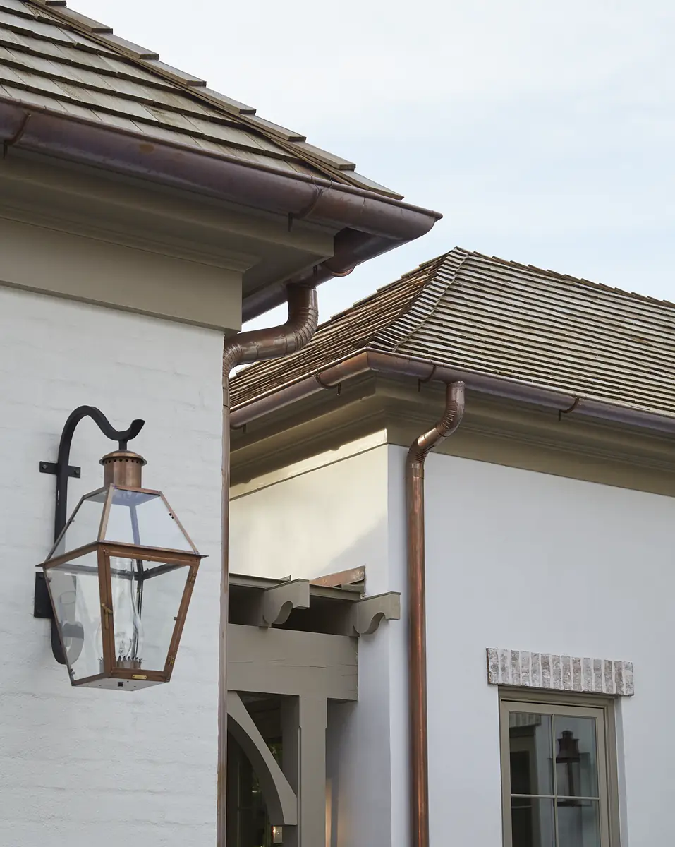 Exterior view of house with white brick, light-colored wall, pitched roofs, lantern, and copper gutters.