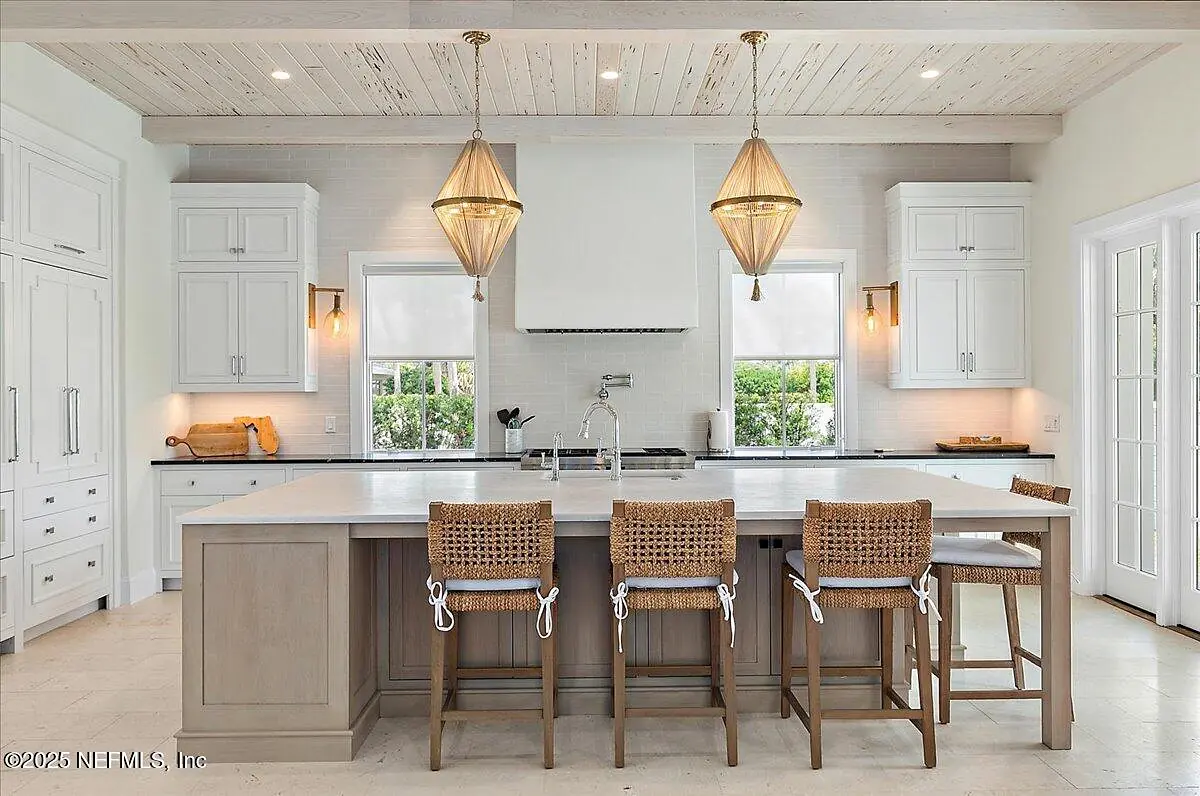 Kitchen with large island, bar stools, white cabinetry, light countertops, and wooden beams.
