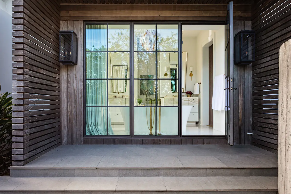 Exterior entrance with large glass door and concrete step, leading to an interior room with furnishings.