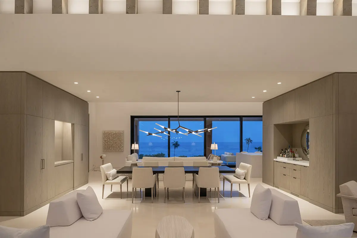 Living room with white furniture, dining table, large window, and built-in cabinetry.