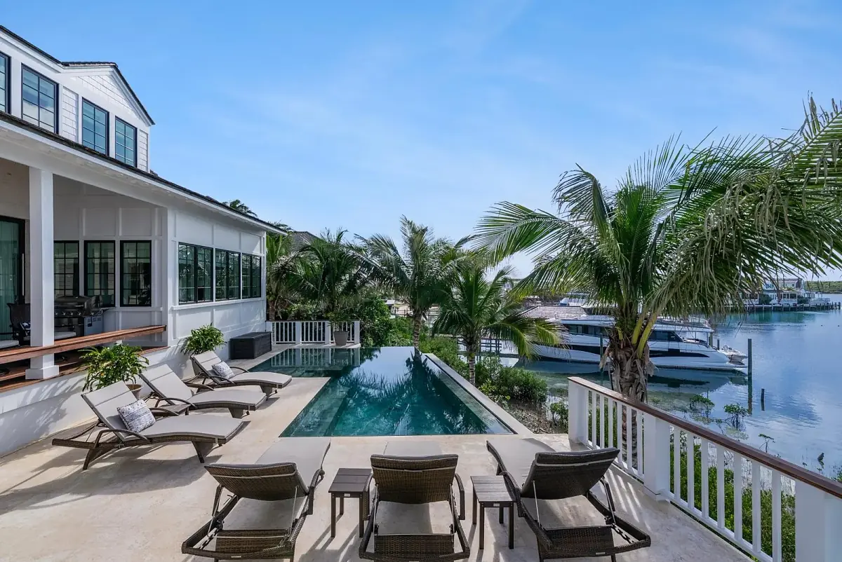 Patio with lounge chairs, infinity pool, palm trees, and marina views.