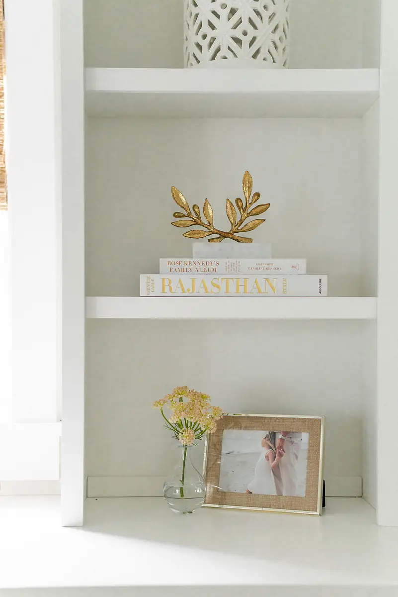 Shelf with decorative items: ceramic piece, stacked books, photo frame, and vase with flowers.