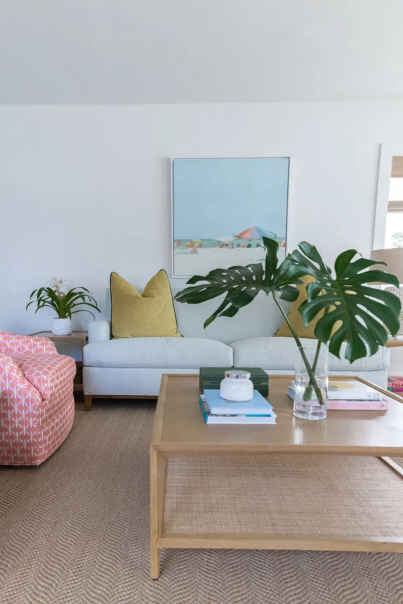 Living room with light blue sofa, yellow cushion, patterned armchair, wooden coffee table, and paintings.