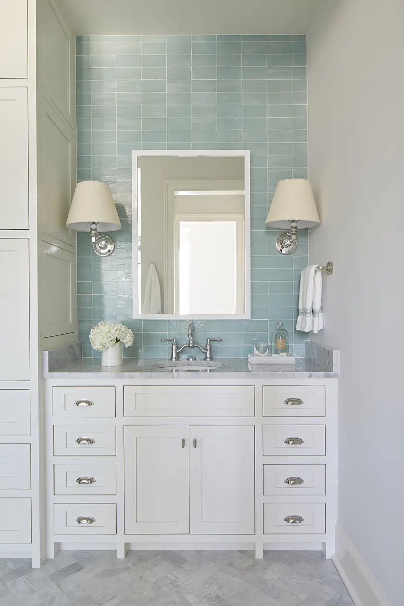 Bathroom with white vanity, marble countertop, light blue tile wall, large mirror, and wall sconces