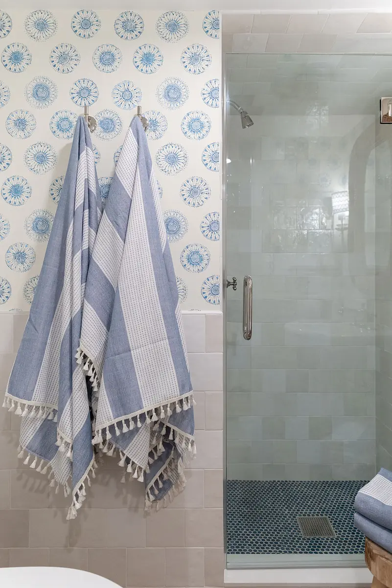 Bathroom with patterned wallpaper, glass shower, blue mosaic tiles, and hanging towels