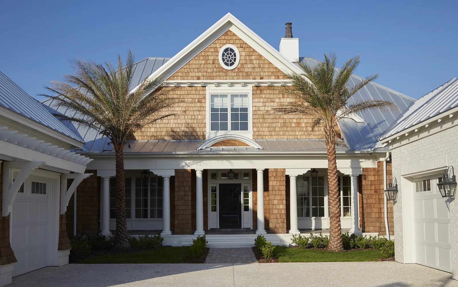 Exterior front of a house with wood shingle siding, double doors, palm trees, and a gravel pathway.
