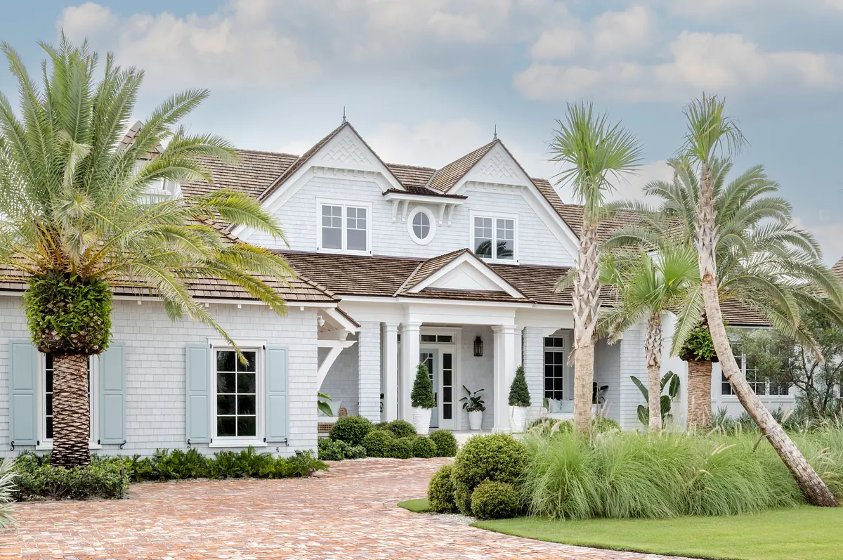 Front exterior with shingle facade, gabled roofs, brick pathway, palm trees, and symmetrical windows.
