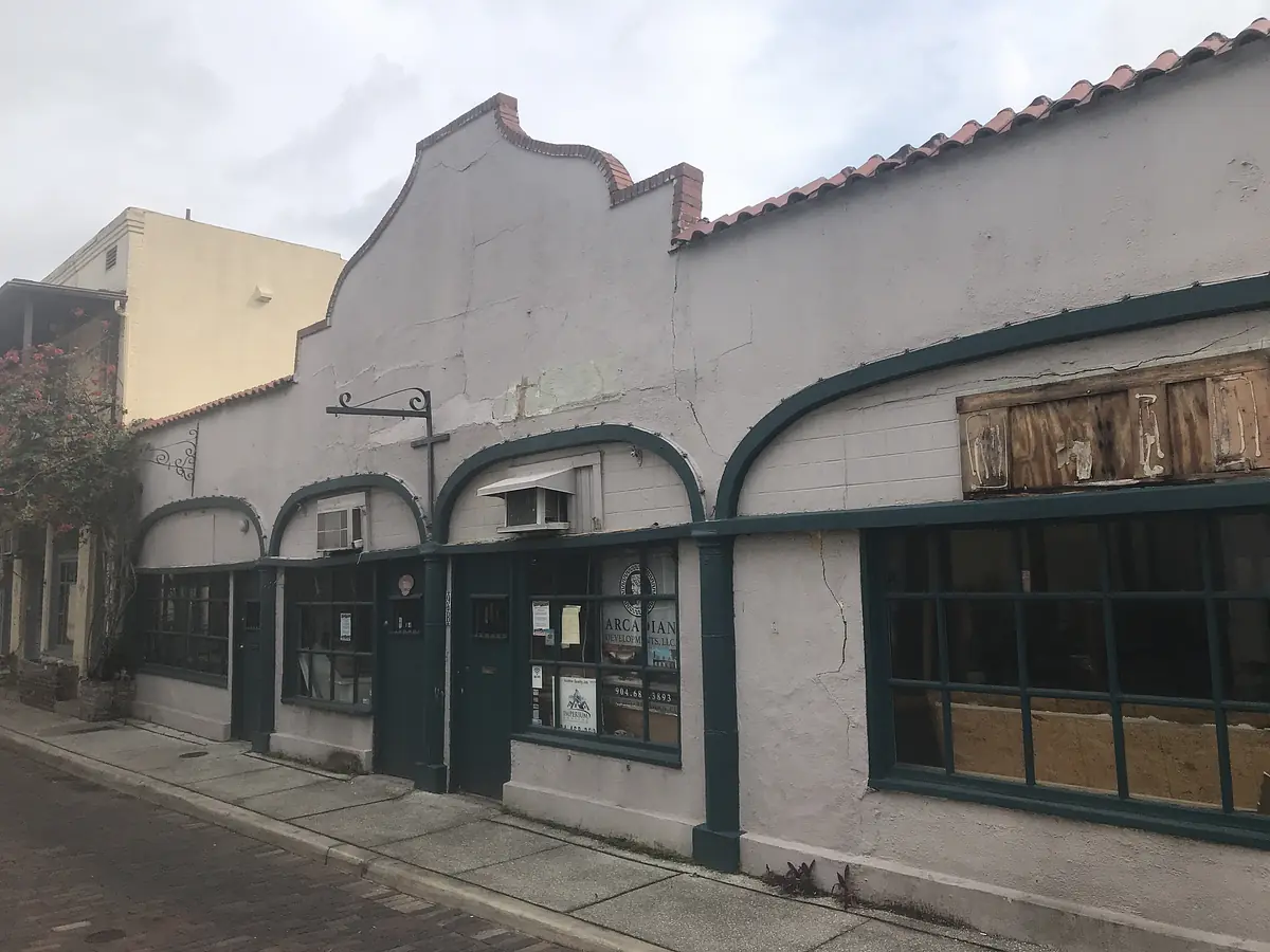 Building facade with stucco walls, arches, large windows, and weathered details.
