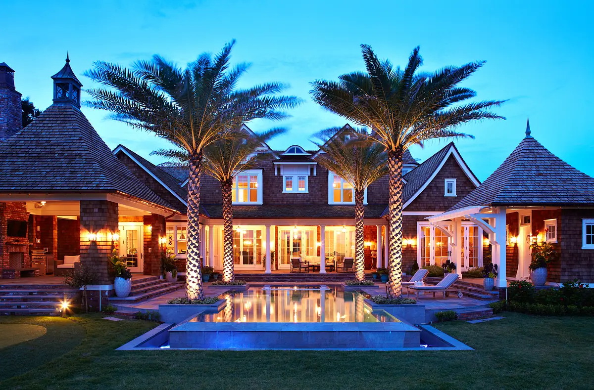 Exterior rear view of a house with a pool, palm trees, landscaped grass, and a deck area.