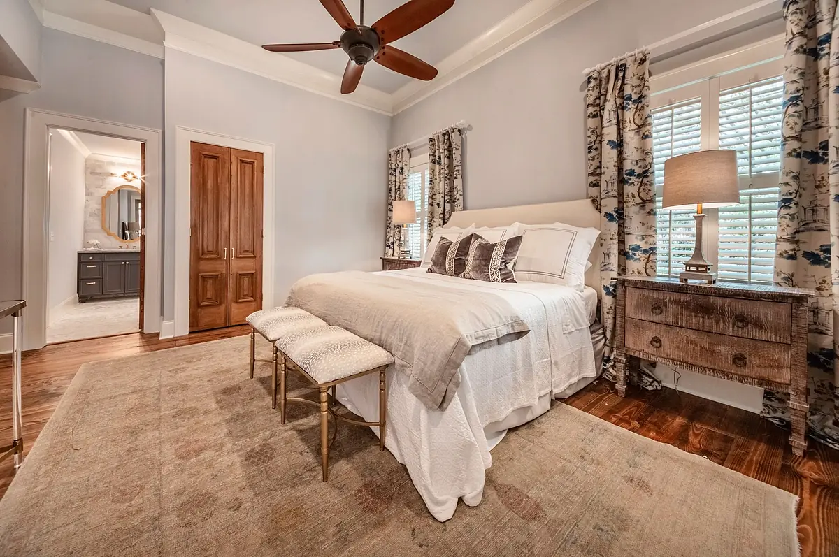 Bedroom with bed, nightstands, lamps, bench, area rug, and floral-patterned curtains.