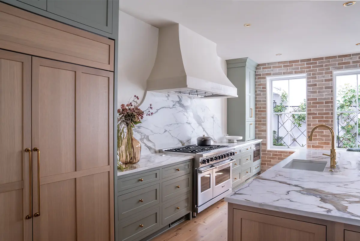 Kitchen with marble countertop, light wood cabinetry, gas range, window, and gold faucet.