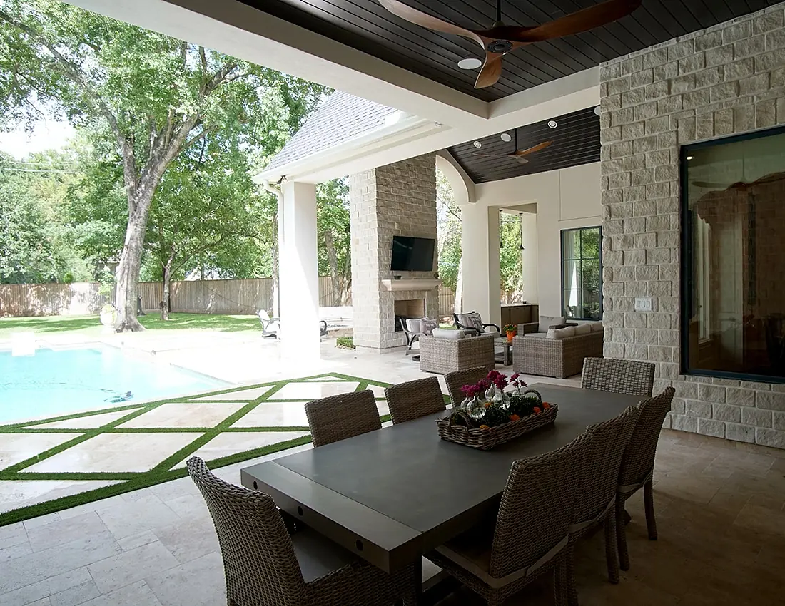 Patio with dining table, wicker chairs, stone fireplace, television, and swimming pool.