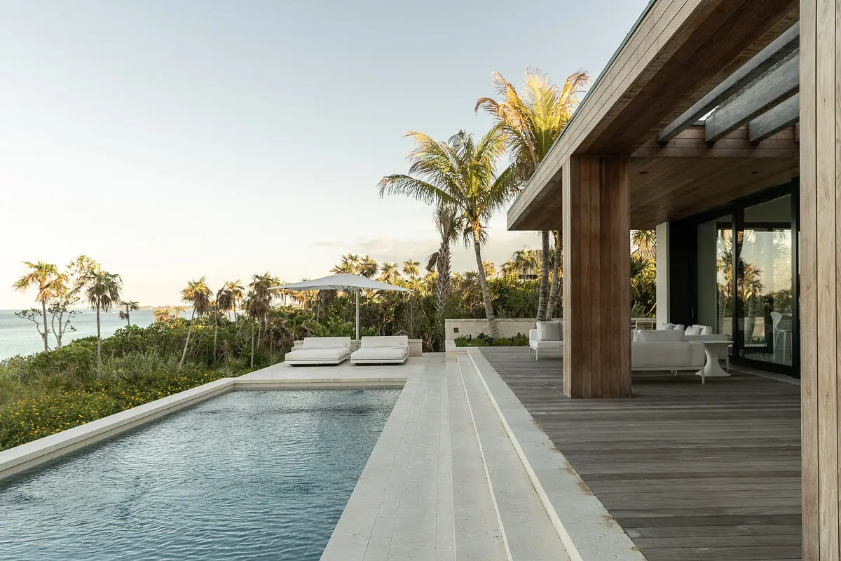 Patio with swimming pool, sun loungers, umbrella, wooden deck, and surrounding greenery.