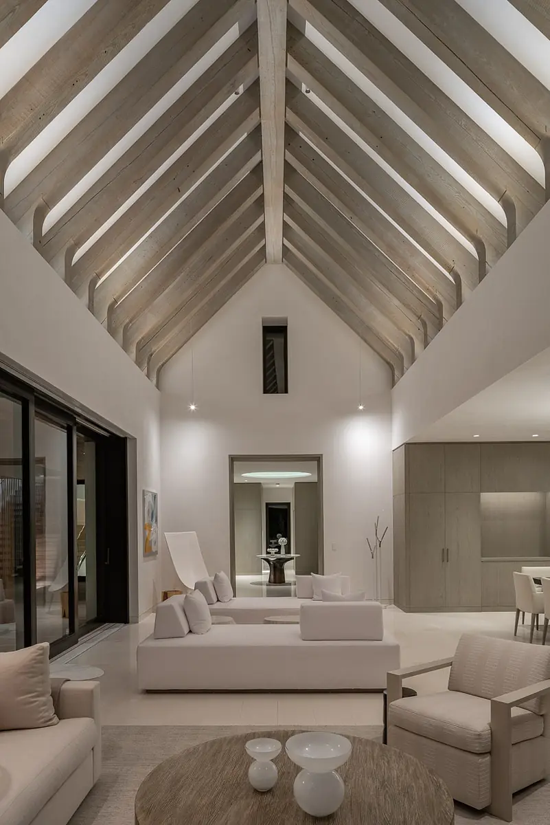 Living room with vaulted ceiling, white sofas, wooden coffee table, area rug, and large glass sliding doors.