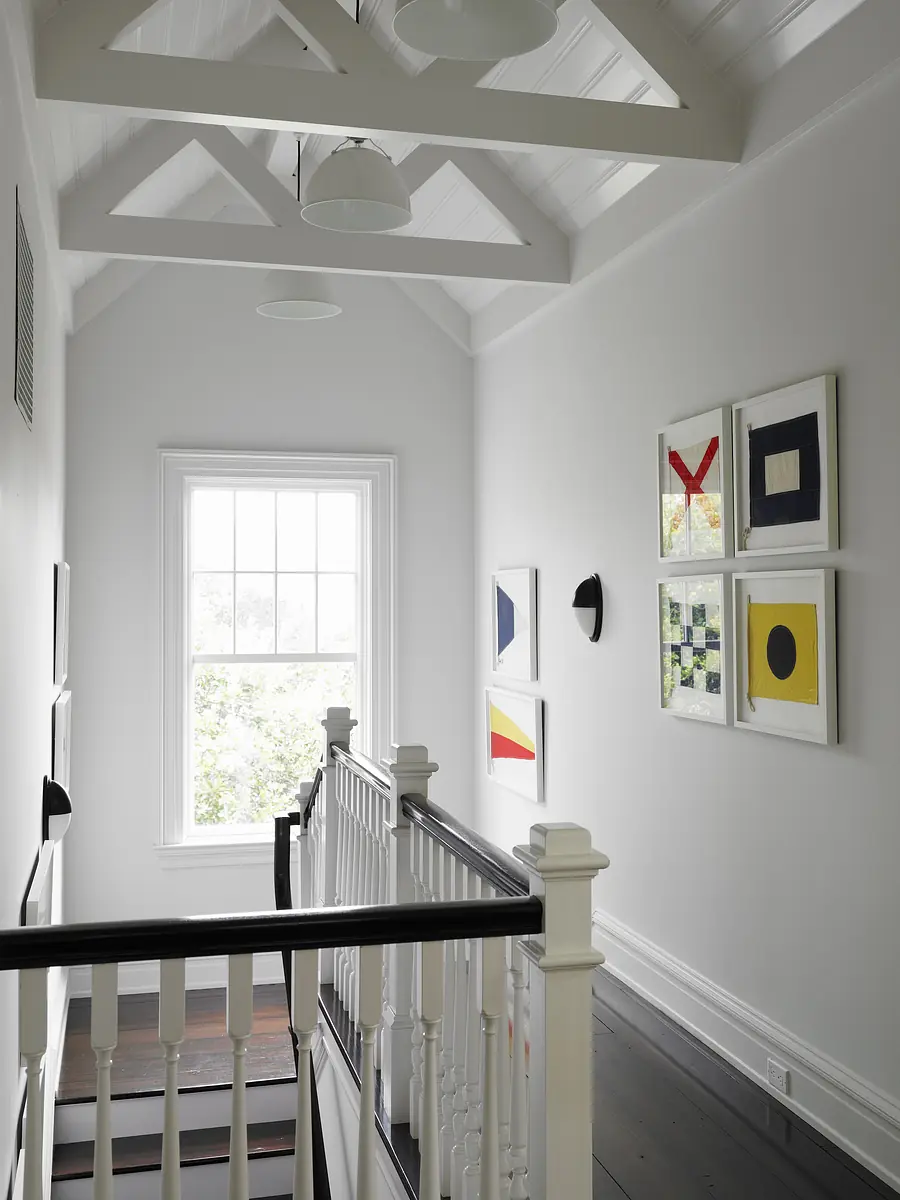 Hallway with white walls, wood staircase, large window, and framed artwork.