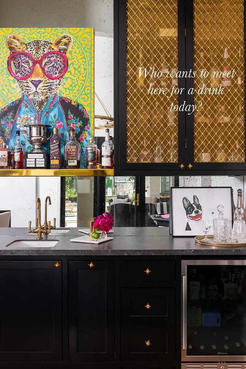 Butler's pantry with dark cabinetry, black countertop, glassware, and a central sink with gold faucet.