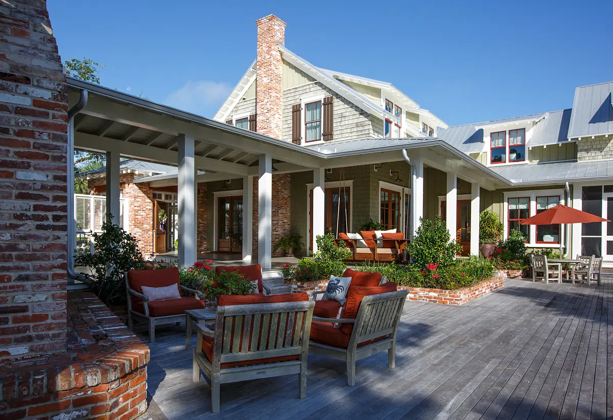 Patio with wooden decking, orange cushioned chairs, table, plants, and an orange umbrella.