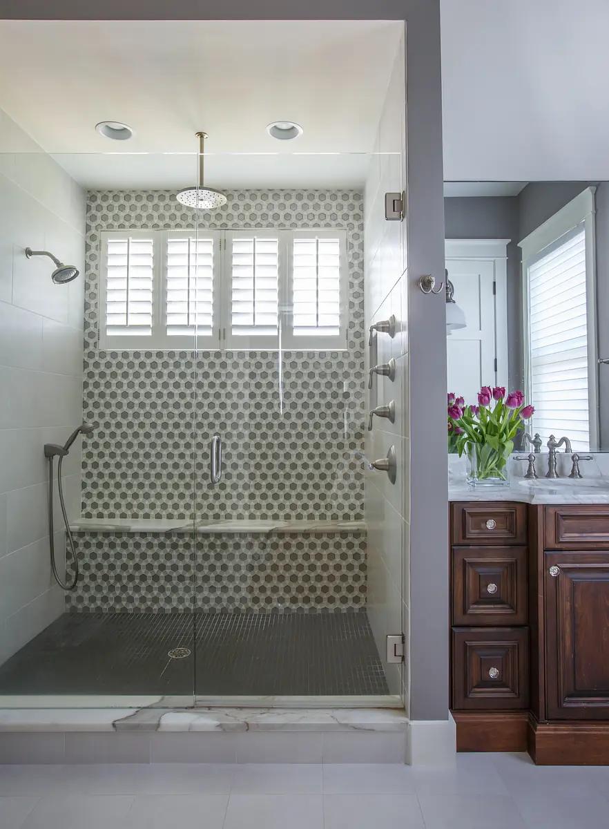 Bathroom with glass shower, tiled wall, dark wood vanity, white sink, and tulips on display