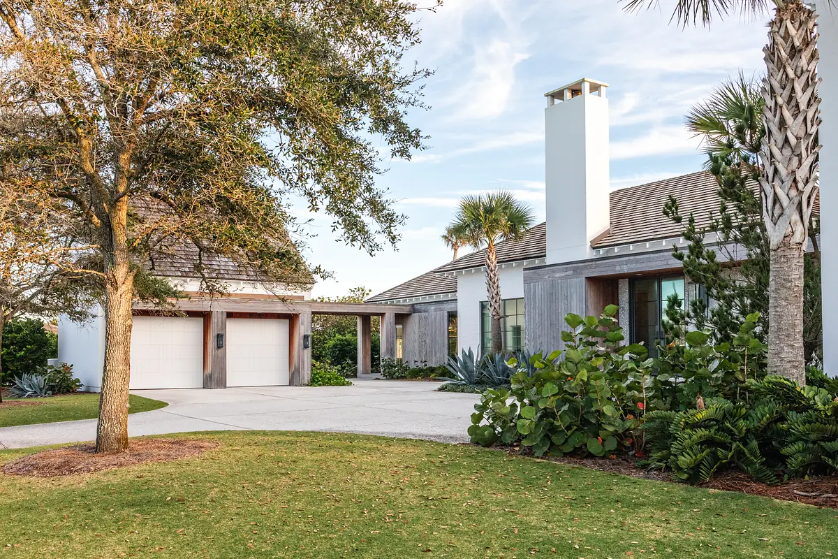 Front exterior view of house with garage, driveway, large windows, and landscaping including palm trees.