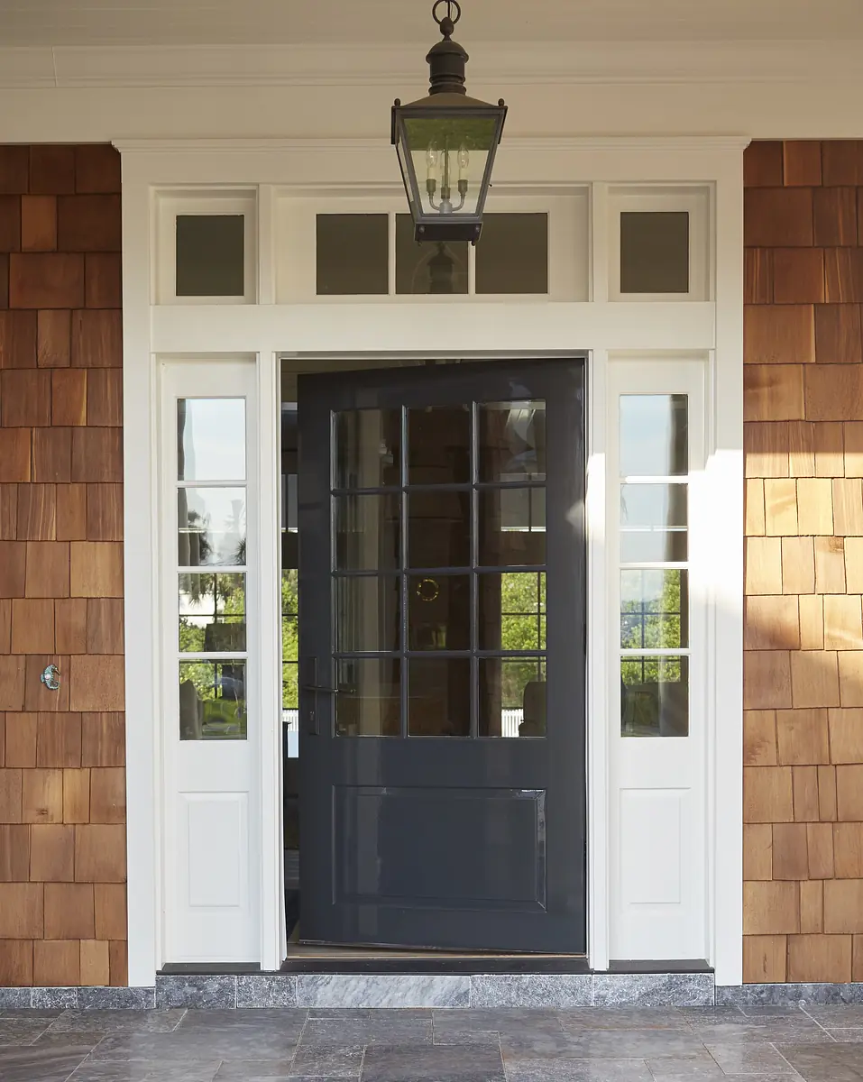 Exterior front entrance with dark wooden door, sidelights, transom window, wood shingles, and stone tiles.