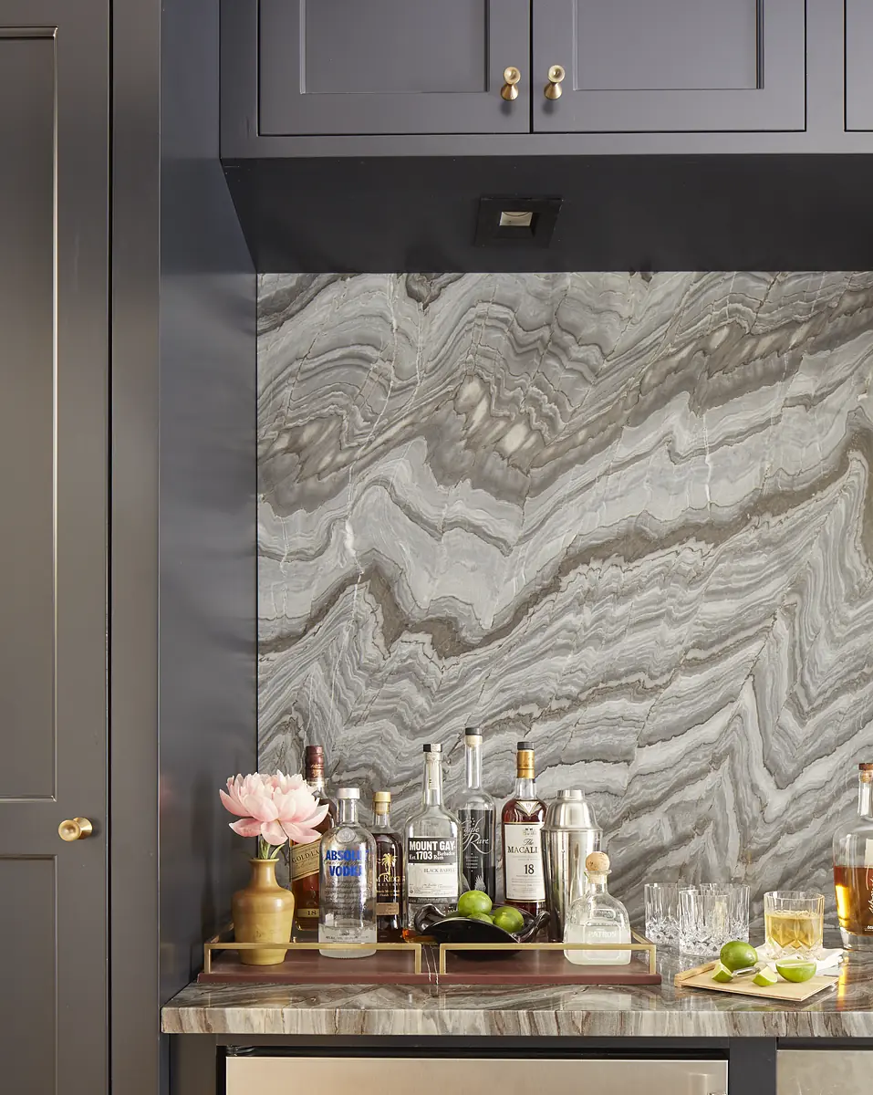 Butler's pantry with gray marble countertop, dark cabinetry, glassware, and decorative tray.