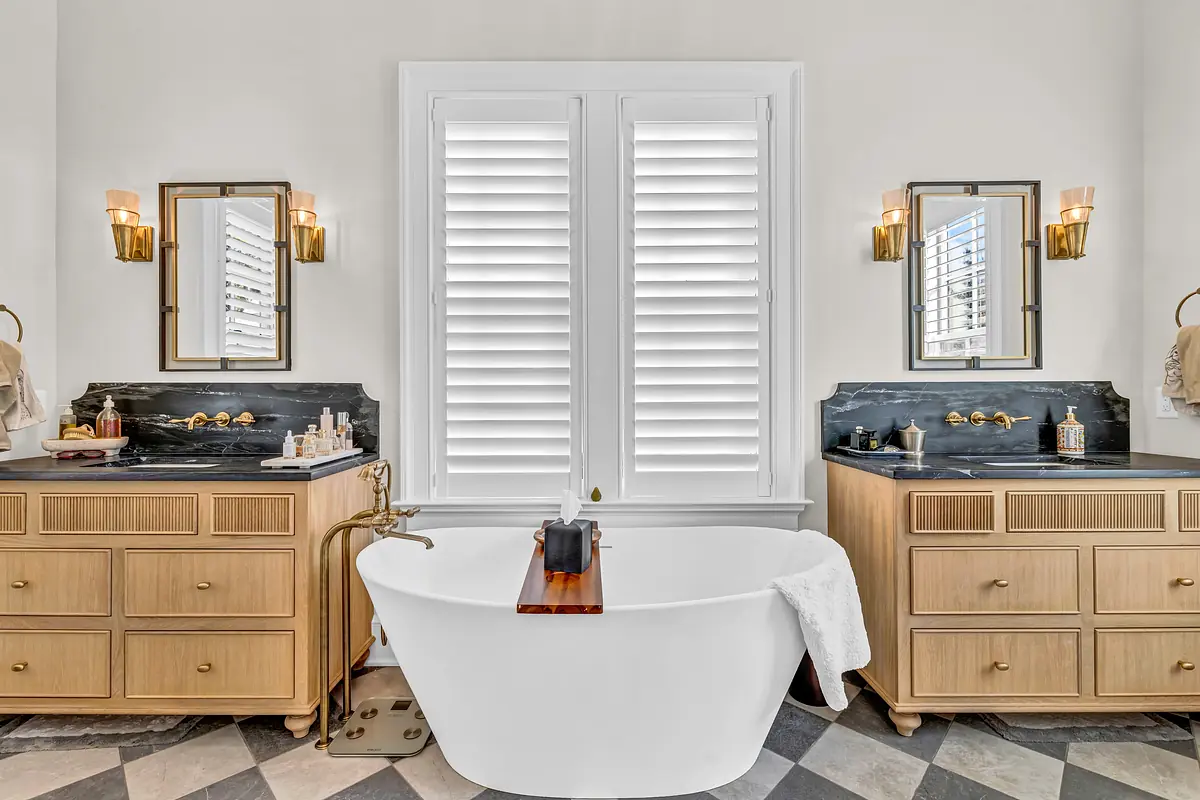 Bathroom with freestanding bathtub, wooden vanities, black countertops, and chevron patterned floor.
